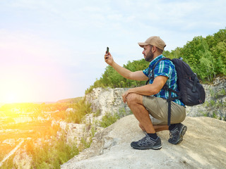 Man tourist is using a smartphone while sitting on the edge of a