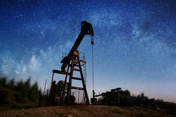 Silhouette of crude oil pump in the night under Starry Sky. Milky way. Petroleum industry equipment