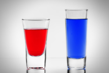 Two blue and red cocktail in full transparent shot glasses with