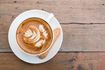 Hot cappuccino in black ceramic cup with beautiful latte art on wooden table.
