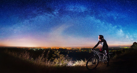 Cross country biker on top of the hill observing beautiful panoramic view of night sky and city...