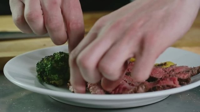 Closeup of male hands putting pieces of medium rare steak on plate with grilled vegetables
