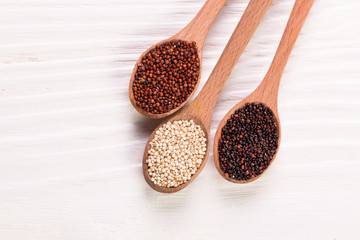 Red, black and white quinoa seeds on a wooden background