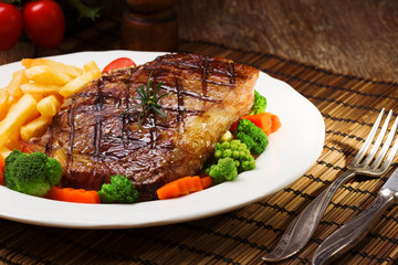 Grilled beef steak served with French fries and vegetables on a