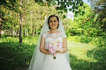 Obraz na płótnie Canvas Portrait of smiled bride with peony wedding bouquet at hands
