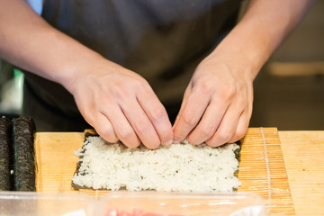 Chef rolling up sushi on a bamboo mat.
