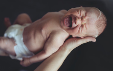 Portrait of newborn baby crying in parents' arms. Mother hands.