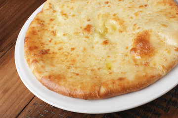 Ossetian pie with potatoes or mutton on a white plate. Wooden background.