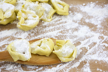 Three raviolis in the flour on the wooden spatula
