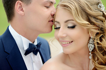 Wedding couple on the nature is hugging each other. Beautiful model girl in white dress. Man in suit. Beauty bride with groom. Female and male portrait. Woman with lace veil. Lady and guy outdoors