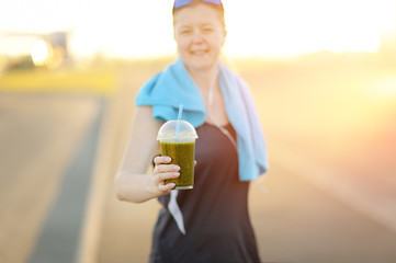 Athletic woman stretches green detox smoothie after workout.