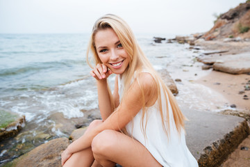 Fototapeta na wymiar Cheerful woman sitting on the rocks near the sea