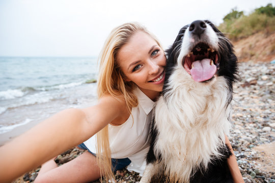Happy woman sitting and making selfie with dog on beach