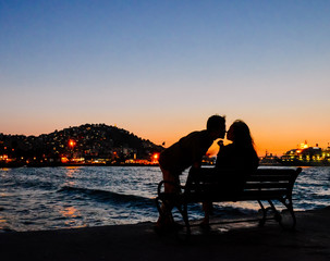 silhouette of young couple kissing on bench in dusk by the sea at Kusadas, Turkey
