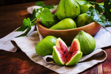 Cut green figs and a wooden bowl of fruit. Vintage wooden backgr