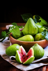 Fototapeta na wymiar Cut green figs and a wooden bowl of fruit. Vintage wooden backgr