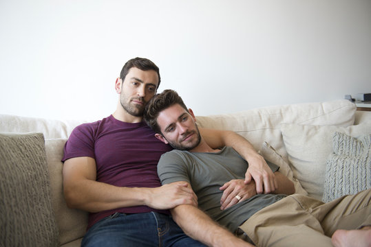 Gay Male Couple On Sofa At Home Watching TV 