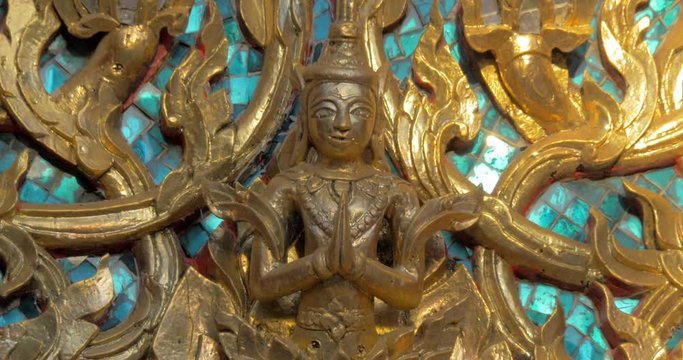 Close-up shot of ornate golden floral pattern and Buddha image on blue mosaic. Decoration detail of Buddhist temple in Bangkok, Thailand