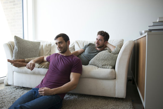Gay Male Couple Relax On Sofa Watching TV 
