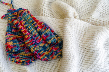 Two multicolored knitted mittens on white scarf