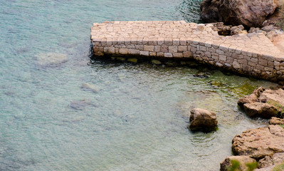 Ancient stone pontoon at turquoise clear water sea shore