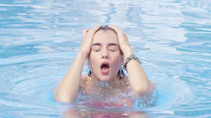 Young woman swimming in a pool just surfacing from the water and wiping back her hair with her hands