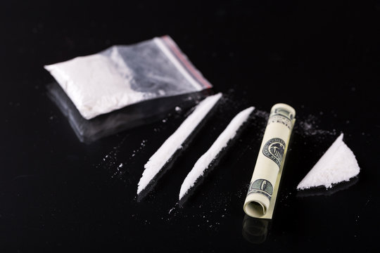 Rolled hundred dollars banknote, two lines and pile of cocaine on black background, closeup 