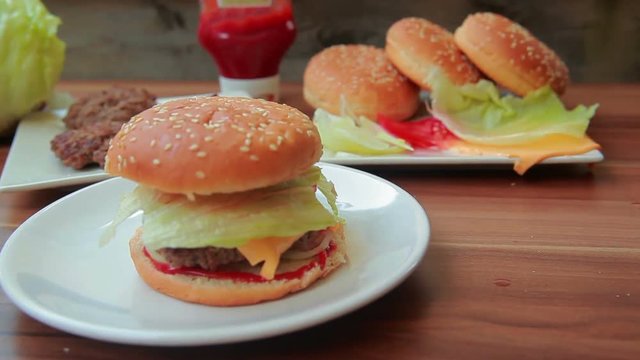 Hand puts tomato and lettuce on a burger