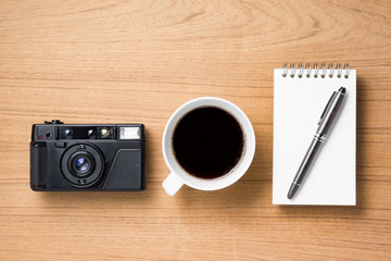 camera coffee cup and pen on note book on wood background