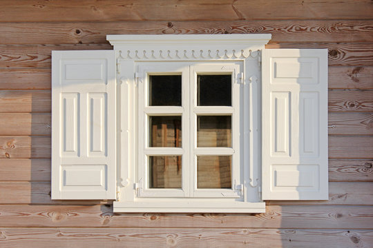Wooden window with beautiful white shutters under olden. Wall of the rural house.