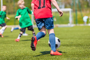 Obraz premium Kids playing football soccer match. Young boys kicking soccer ball on sports field. Youth sport competition