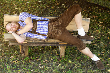 young man in traditional bavarian clothes sleeping on bench