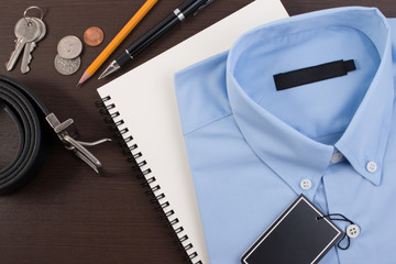 Accessories: Classic shirt with black blank price tag, belt, pencil, pen and coins on wooden table.