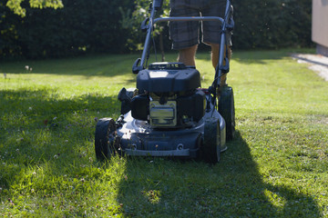Man cutting grass by lawn mower, powerful petrol lawn mower in sunlight