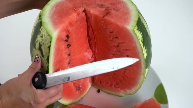 Girl cut ripe watermelon with a knife on a white table. Slow motion