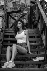 Young charming leggy girl with curly hair in a white shirt and red shorts sitting on the wooden stairs near the fortress in Lviv during a walk on a warm summer sunny day