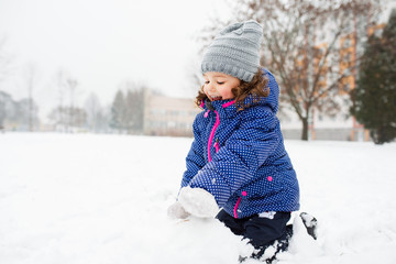 Little girl building a snowman in winter nature