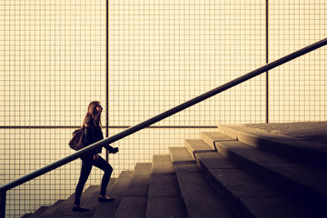 Young girl walking up stairs in a city environment, modern square tiles on background. Space for...