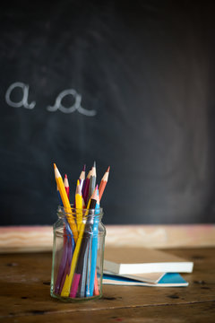 crayons de couleur dans un pot et des cahiers devant un tableau noir