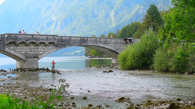 A fisherman is fishing under the bridge, fly fishing. Mountain river and mountain lake Bohinj, Slovenia.