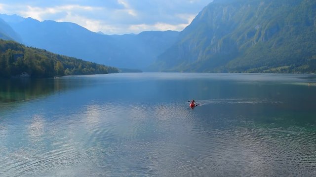 Lake Bohinj, Slovenia, two people traveling by kayak. The mountain lake at mountain background. Sunny sky with clouds. Alps landscape background.