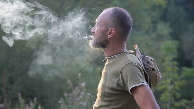 Smoker in nature in a puff of smoke. Man lighting cigarette in garden. 