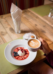 Woman with cup of coffee and white milky creamy pudding with jam and berries blueberries, strawberry, raspberry in cafe or restaurant. Close-up