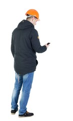 Backview of an engineer in construction helmet stands and using a mobile phone. Standing young guy. Rear view people collection.  backside view of person.  Isolated over white background.