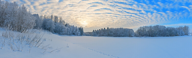 Wavy clouds over snowy river and forest in frost.