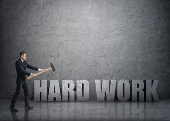 Obraz premium Side view of young businessman crashing 3D concrete 'hard work' words with a hammer
