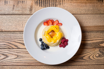Creamy pudding with white sauce and berries blueberries, strawberry, raspberry on a white plate at...