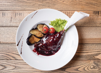 Roast duck or goose leg crisp delicious in red cranberry sauce served with garnish eggplant, fresh tomatoes and lettuce on a white plate