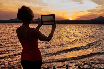Girl photographing the sunset on the table - obrazy, fototapety, plakaty