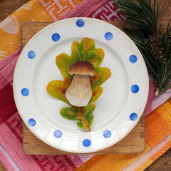 White mushroom and yellow oak leaf on a vintage plate, top view.
